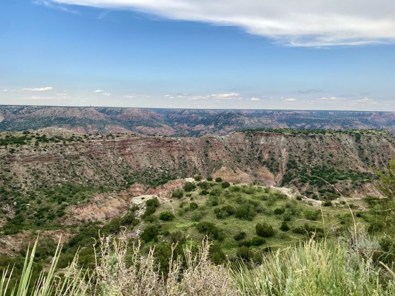 Stunning landscape of Palo Duro Canyon, featuring towering red cliffs and winding trails amidst the rugged terrain.