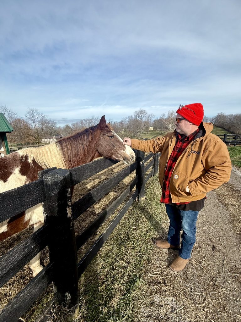 man petting horse next to a fence
